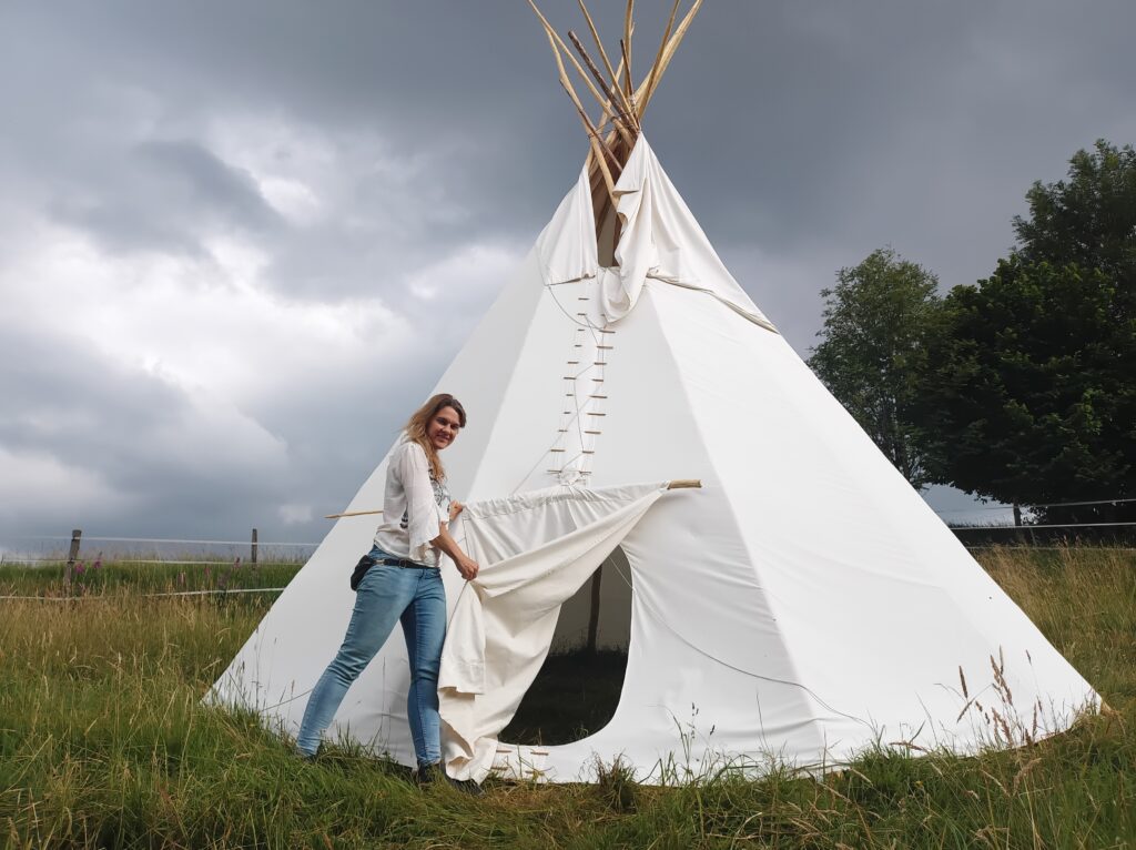 Natalie steht vor Tipi und hält den Stoff der Türe auf